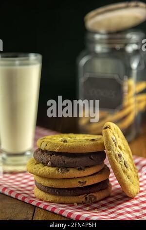 Pila di biscotti al cioccolato su panno rosso di gingham con vetro del latte e del vasetto di biscotti Foto Stock