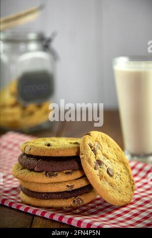 Pila di biscotti al cioccolato su panno rosso di gingham con vetro del latte e del vasetto di biscotti Foto Stock