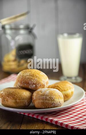 Piatto di ciambelle di marmellata su panno rosso di gingham con vetro del latte e del vasetto di biscotti Foto Stock