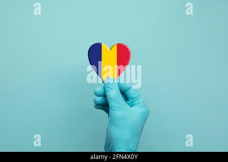 Mani che indossano guanti chirurgici protettivi che tengono il cuore bandiera Romania Foto Stock
