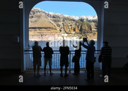 Santorini, Grecia, 04 ottobre 2017. Vista dell'avvicinamento al porto e al porto di Santorini dalla nave da crociera con figure silhouted di passeggeri che scattano foto che mostrano le scogliere con la città dipinta di bianco sopra Foto Stock