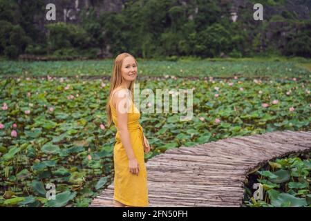 Giovane donna in abito giallo sul sentiero tra il lago di loto. MUA Cave, Ninh Binh, Vietnam. Il Vietnam riapre dopo la quarantena Coronovirus COVID 19 Foto Stock