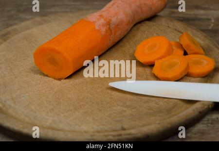 tagliare carote, su piatto e tavola di legno con coltello in ceramica per insalata naturale e biologica. cibo sano Foto Stock