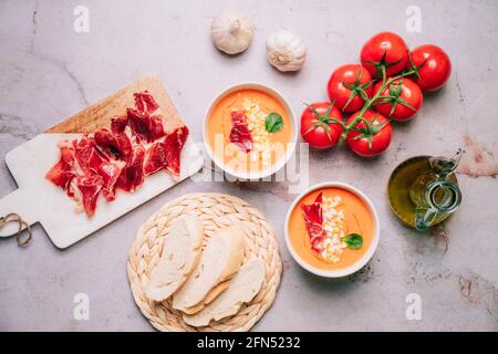 Salmorejo - zuppa spagnola di pomodoro gazpacho in due ciotole con prosciutto e uovo bollito e gli ingredienti su un tavolo di marmo. Vista dall'alto o piatta Foto Stock