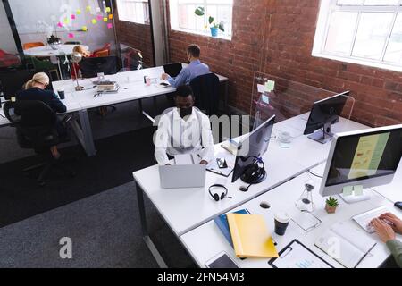 Vista dall'alto dell'uomo afro-americano che indossa una maschera facciale con computer portatile in ufficio Foto Stock