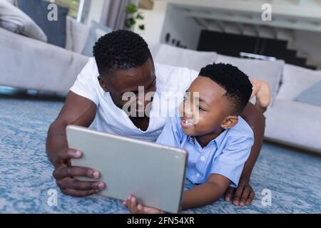 Padre e figlio afro-americano seduto a terra, usando un tablet e sorridendo Foto Stock