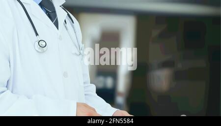 Composizione della sezione centrale del medico maschile in camice di laboratorio con stetoscopio oltre l'ospedale fuori fuoco Foto Stock