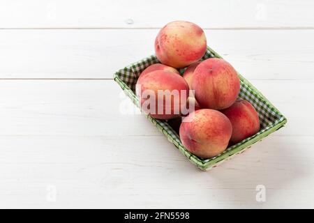 Pesche fresche e mature in un cestino su sfondo bianco di legno. Frutta deliziosa e sana. Concetto di cibo sano. Foto Stock