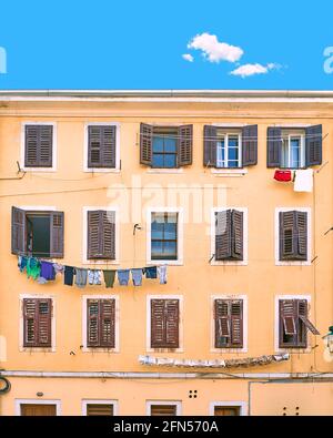 Pittoresca casa residenziale tipica italiana in slum sotto un cielo estivo blu con una nuvola unica in Italia. Parete con molte finestre con persiane e. Foto Stock