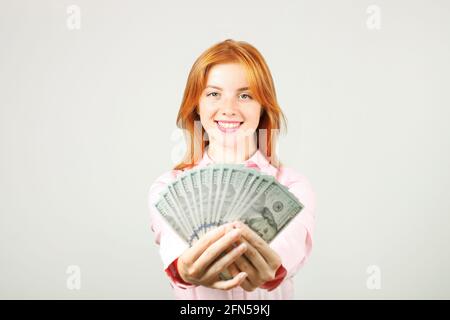 Ritratto di giovane bella donna rossa con pugnale di soldi che tengono uno stack di bolletta di cento dollari come ventilatore. Eccitata attraente rosso capelli femmina con/ Foto Stock