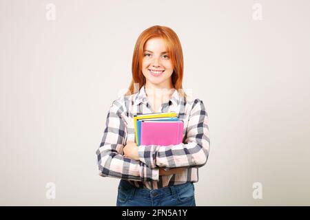 Giovane bella donna con testa rossa naturale lunga con camicia a scacchi in flanella che tiene un mazzo di taccuini e sorridente. Redhead femmina college studien Foto Stock