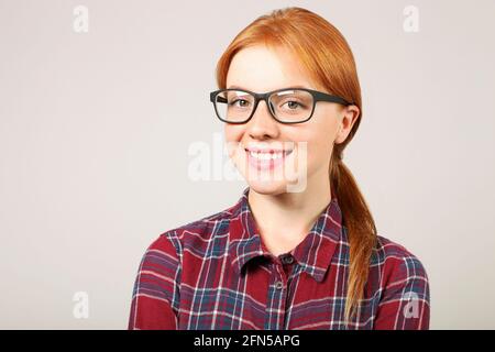 Primo piano ritratto di bella studentessa giovane donna college con capelli rossi che indossano occhiali neri cornice e camicia flanella. Rosso femmina sorridente. Redhea Foto Stock