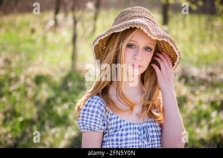 Bella ragazza bionda teen all'aperto in spoglietta e cappello da sole, retroilluminata. Foto Stock