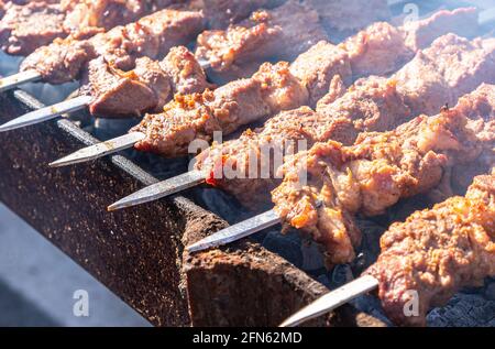 Grigliata appetitosa cucina kebab su spiedini di metallo, primo piano. Shashlik durante la cottura sul mangal su saloni caldi, cibo di strada. Messa a fuoco selettiva Foto Stock