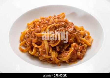 Tagliatelle italiane condite con salsa di carne e pomodoro, primo piano in un piatto bianco Foto Stock