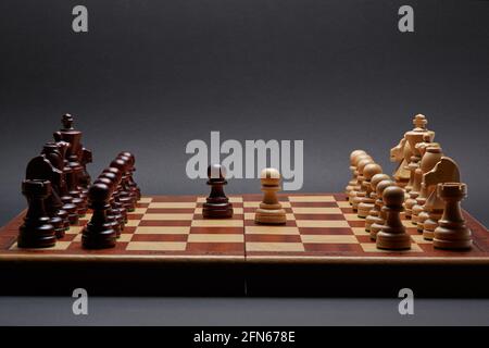 Classico torneo di scacchi in legno ambientato su sfondo nero. Due pedine al centro della tavola altri pezzi allineati Foto Stock