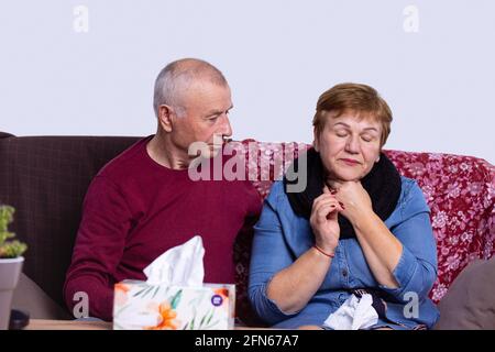 Uomo dai capelli grigi che si prende cura del coniuge malato a casa. Donna che ha freddo e mal di gola dal condizionatore d'aria, scatola di tovaglioli sul tavolo. Concetto di assistenza sanitaria Foto Stock