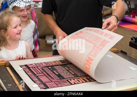 Le sorelle guardano la stampa fatta a mano su una stampa di un poster per celebrare Art in Action Festival Waterperry House, Oxfordshire, Regno Unito, nel luglio 2016. (123) Foto Stock