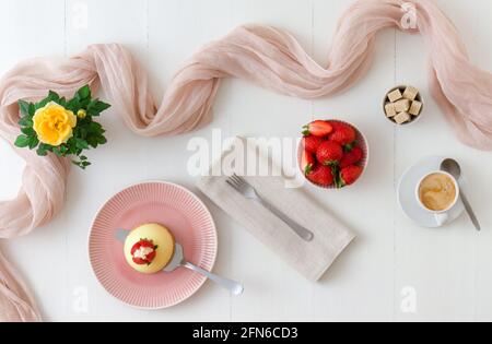 Cupola fatta in casa di torta di formaggio al limone senza forno con fragole fresche. Tavolo di legno bianco con rosee gialle sullo sfondo. Foto Stock