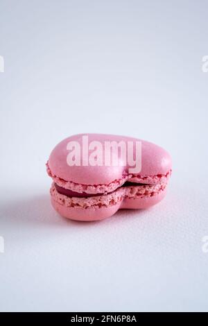 Un singolo macaron francese a forma di cuore aromatizzato alla fragola, spazio di copia su sfondo neutro, verticale Foto Stock