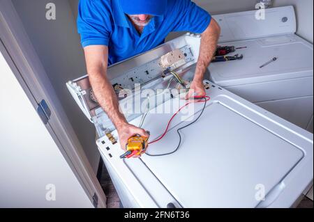 Tecnico dell'apparecchio o addetto alla riparazione che lavora sui circuiti di una capote caricare la lavatrice all'interno di una casa residenziale Foto Stock
