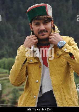 Ritratto di un bel ragazzo giovane che regola il suo collare della giacca, UN ragazzo giovane che indossa una giacca gialla e himachali topi (cappellino tradizionale Himachal) Foto Stock