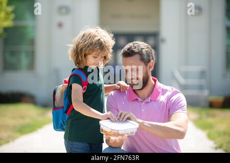 Pranzo scolastico per bambini. Il Padre sostiene e motiva il figlio. Scolaro e genitore in camicia che tiene il pranzo al sacco. Foto Stock