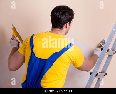 Il giovane dipendente del contraente di applicare gesso sulla parete Foto Stock