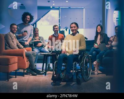 Ritratto di una donna d'affari disabile su una sedia a rotelle di fronte il suo team aziendale in ufficio Foto Stock