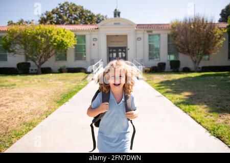 Ritratto del bambino che corre sul parco giochi alla fine della classe. Divertente felice scuola ragazzo faccia. L'inizio delle vacanze. Immagini dinamiche che tornano a. Foto Stock