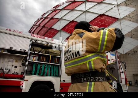 Mosca, Russia. 14 maggio 2021. Di fronte a un camion dei vigili del fuoco e all'edificio dello stadio di calcio Otkritie Arena a Mosca, in Russia, si trova un vigile del fuoco. Lo stadio di calcio Otkritie Arena è sede della squadra di calcio Spartak Foto Stock