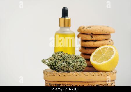 Dolci con olio CBD. Gemme di marijuana su sfondo bianco. Primo piano fiori di cannabis e biscotti al cioccolato. Foto Stock