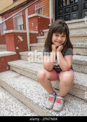 Sorridente bambina seduta sui gradini anteriori di a. porta in una giornata estiva Foto Stock