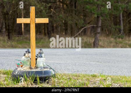 Una croce commemorativa a lato della strada con candele che commemorano la tragica morte accanto a una strada. Foto Stock