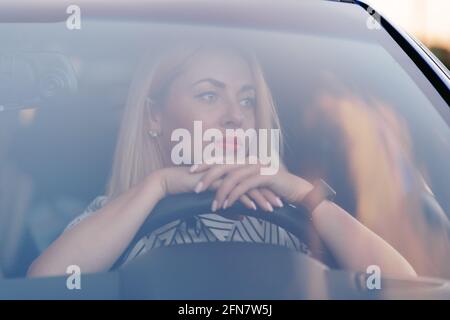 Ritratto di signora in auto. Giovane bella donna che guida. Vista frontale attraverso il parabrezza con luce solare. Foto Stock