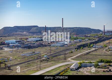 Vista aerea su stazione ferroviaria, strada, pile di fumo di lavorazione e impianto termoelettrico, e discariche minerarie all'orizzonte. Cielo blu. Foto Stock