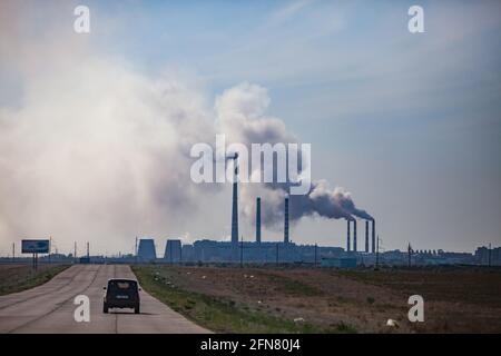 Pavlodar, Kazakhstan strada in lastre di cemento con auto. Silhouette della centrale elettrica all'orizzonte. Cielo nuvoloso grigio. Foto Stock