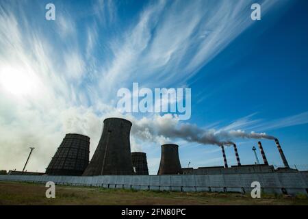 Silhouette vista panoramica sulla centrale termica Pavlodar. Torri di raffreddamento lato sinistro. Pile di fumo con diritto fumo bianco. Cielo blu con nuvole. Foto Stock