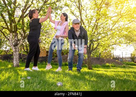 Felice, positivo sorridente famiglia che gioca a bocce di gioco tradizionale francese in giardino all'aperto durante la bella giornata estiva, godendo di tempo libero Foto Stock