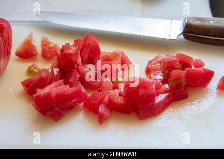 pomodori di primo piano tritati su tagliere bianco con coltello da cucina. fuoco selettivo. Foto Stock