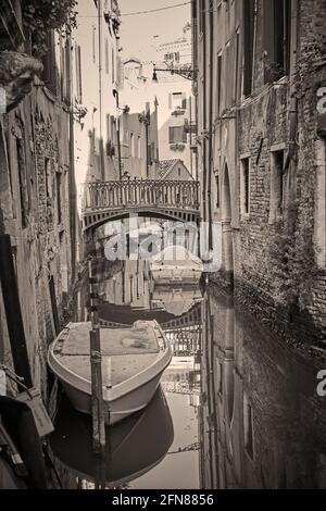 Canale a Venezia con ponte e barche, Italia. Fotografia in bianco e nero in stile vintage, vista veneziana in tonalità seppia Foto Stock