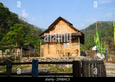 Grazioso cottage giallo con recinzione in legno nero e tetto di paglia, cielo blu nuvoloso e verde collina himalayan. Foto Stock