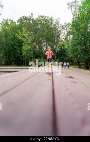 bambina che cammina su un sentiero in legno nel parco dopo la pioggia, copia spazio. Profondità di campo poco profonda Foto Stock