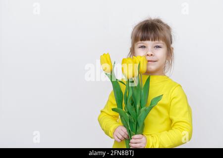 carino bambina in una blusa gialla con tulipani gialli su uno sfondo grigio, copia spazio Foto Stock