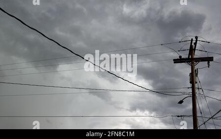 Infrastruttura di rete elettrica, polo di servizio e linee di alimentazione aeree con nuvole e un cielo tempestoso Foto Stock