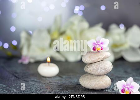 Composizione terapeutica del resort termale. Pietre, candele brucianti, fiori di orchidea, asciugamano, luci astratte Foto Stock