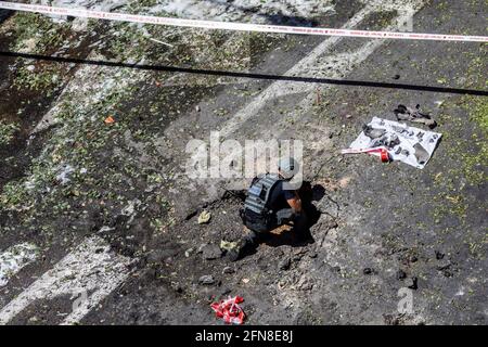 Ramat Gan, Israele. 15 maggio 2021. Un membro delle forze di sicurezza ispeziona un buco che è stato colpito da un razzo sparato dal movimento islamico palestinese Hamas da Gaza verso Israele, in mezzo all'escalation della violenza israelo-palestinese. Credit: Ilia Yefimovich/dpa/Alamy Live News Foto Stock