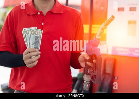 Concetto di risparmio sui costi del carburante, mano del lavoratore del personale che trattiene denaro contante presso la stazione di servizio Foto Stock