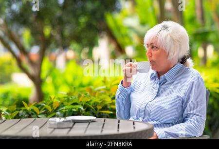 Donna premurosa che si rilassa con una tazza di tè o caffè su un patio esterno con lussureggianti piante tropicali una vista ravvicinata sulla tabella Foto Stock