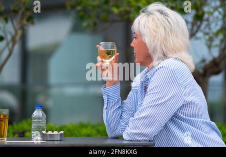 Donna che gusterà un aperitivo di vino bianco in un ristorante all'aperto tavolo come lei si siede guardando pensieroso fuori al lato con copyspace Foto Stock